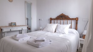Ein ordentlich bezogenes Bett mit weißen Bettwäsche und Handtüchern, ein hölzernes Kopfteil, ein Nachttisch mit Lampe sowie ein Spiegel an der Wand.