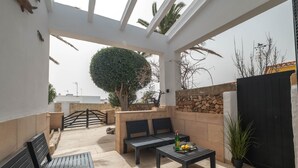 Ein Außenbereich mit Terrasse, einer Steinsäule, einem schwarzen Tor, einem Baum mit runder Krone und einem Tisch mit Zitronen.
