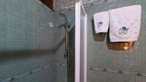 A bathroom with green tiled walls, a shower, and two towels with floral embroidery.