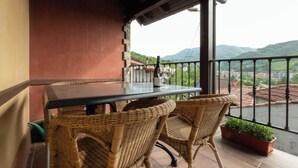A balcony with wicker chairs, a table, and a potted plant.