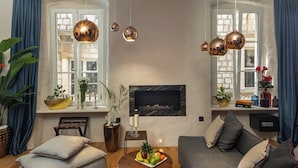 Ein gemütliches Wohnzimmer mit Kamin, einer Couch, einem Esstisch mit Obst und hängenden Kupfer-Pendelleuchten.