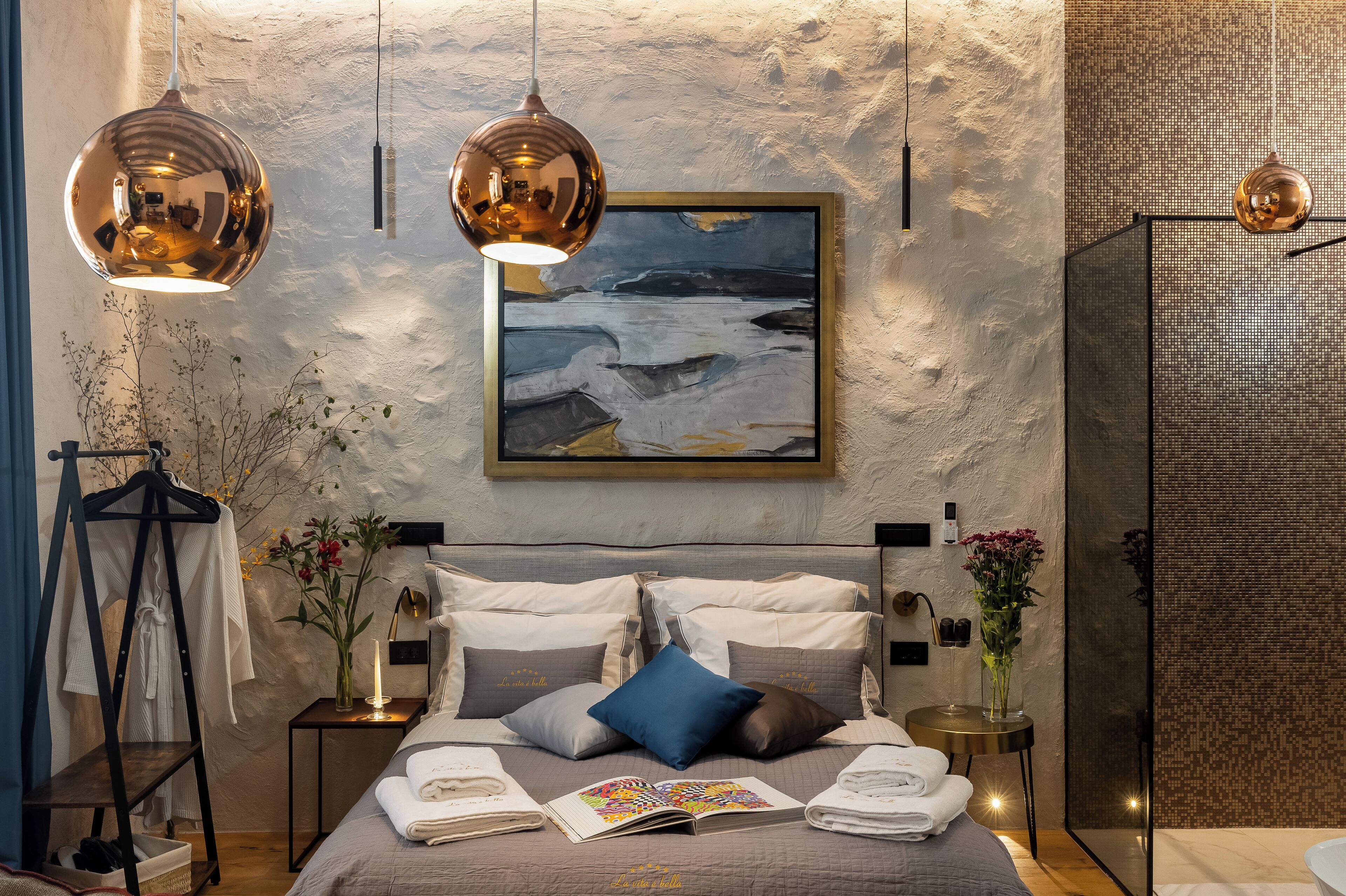 Un dormitorio moderno con una cama grande, dos lámparas colgantes, un cuadro y una mesita de noche con un florero.