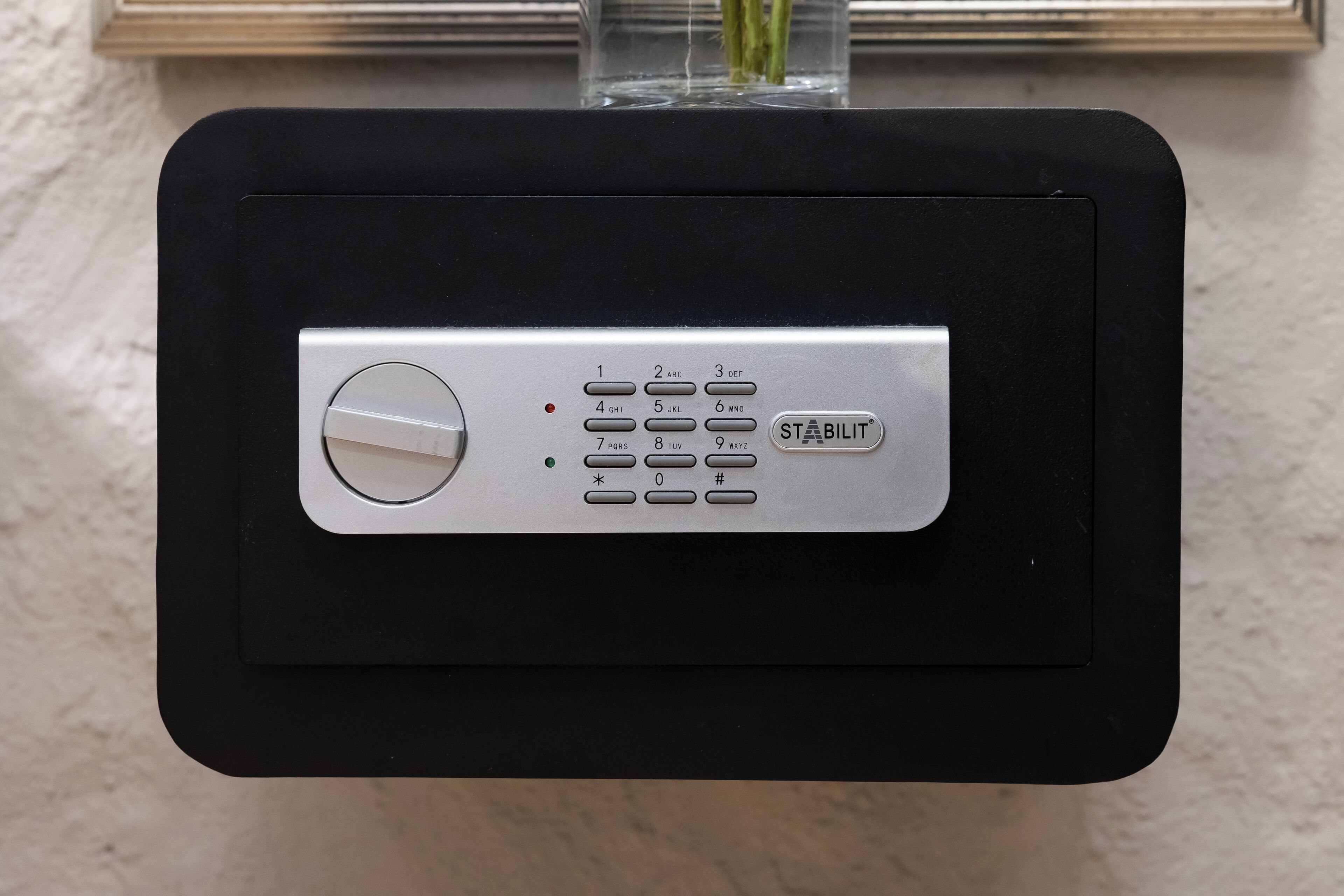 A black electronic device with a keypad and a control button, mounted on a wall.