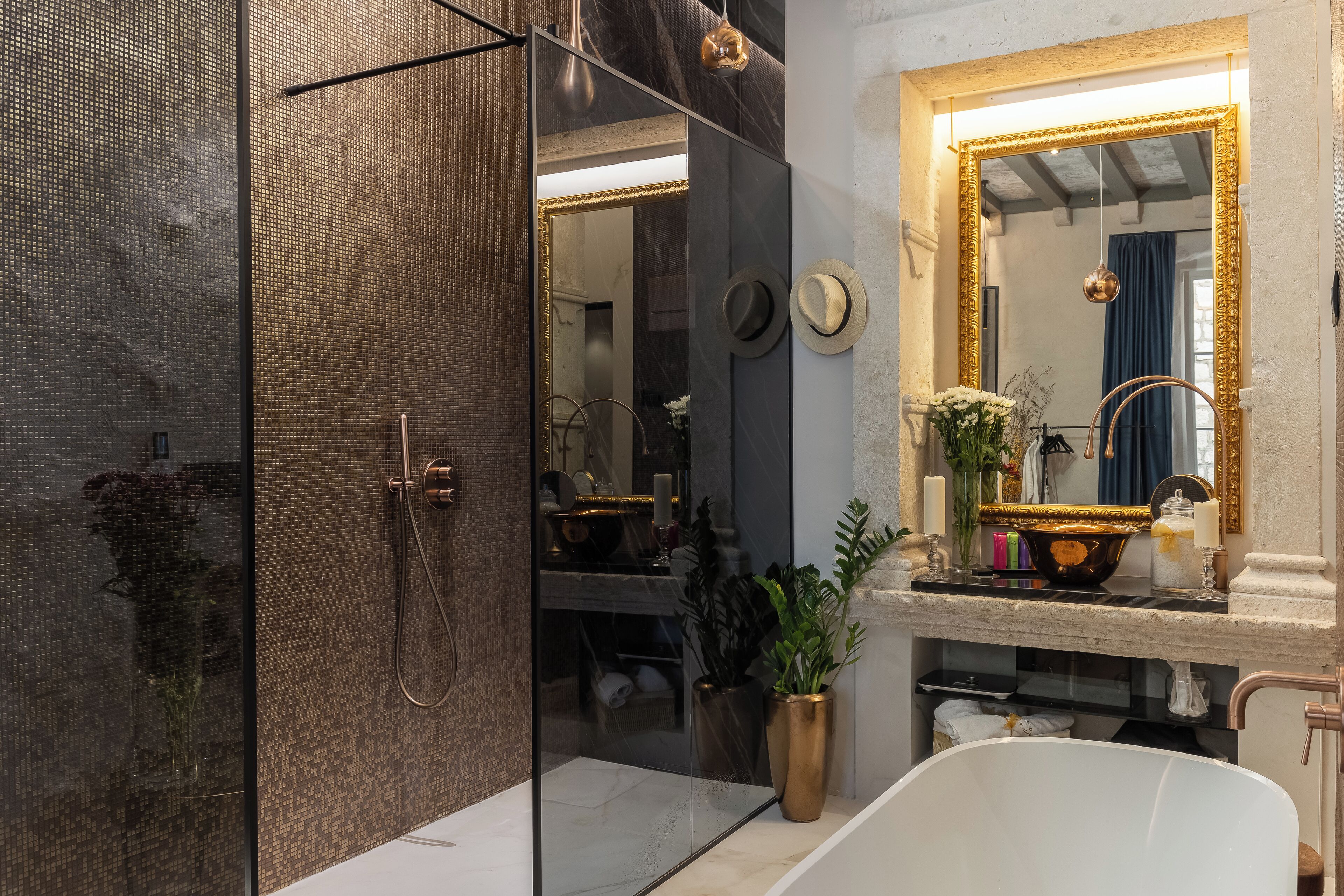 Ein modernes Badezimmer mit einer Duschkabine, einem großen Spiegel mit goldener Rahmung und einer weißen Badewanne.