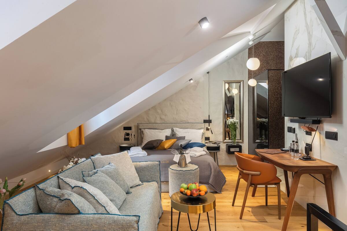 Une chambre de style loft moderne, avec un plafond en pente, un grand lit, un bureau et un téléviseur.