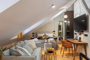 Quarto estilo loft moderno com teto inclinado, uma cama grande, uma escrivaninha e uma televisão.