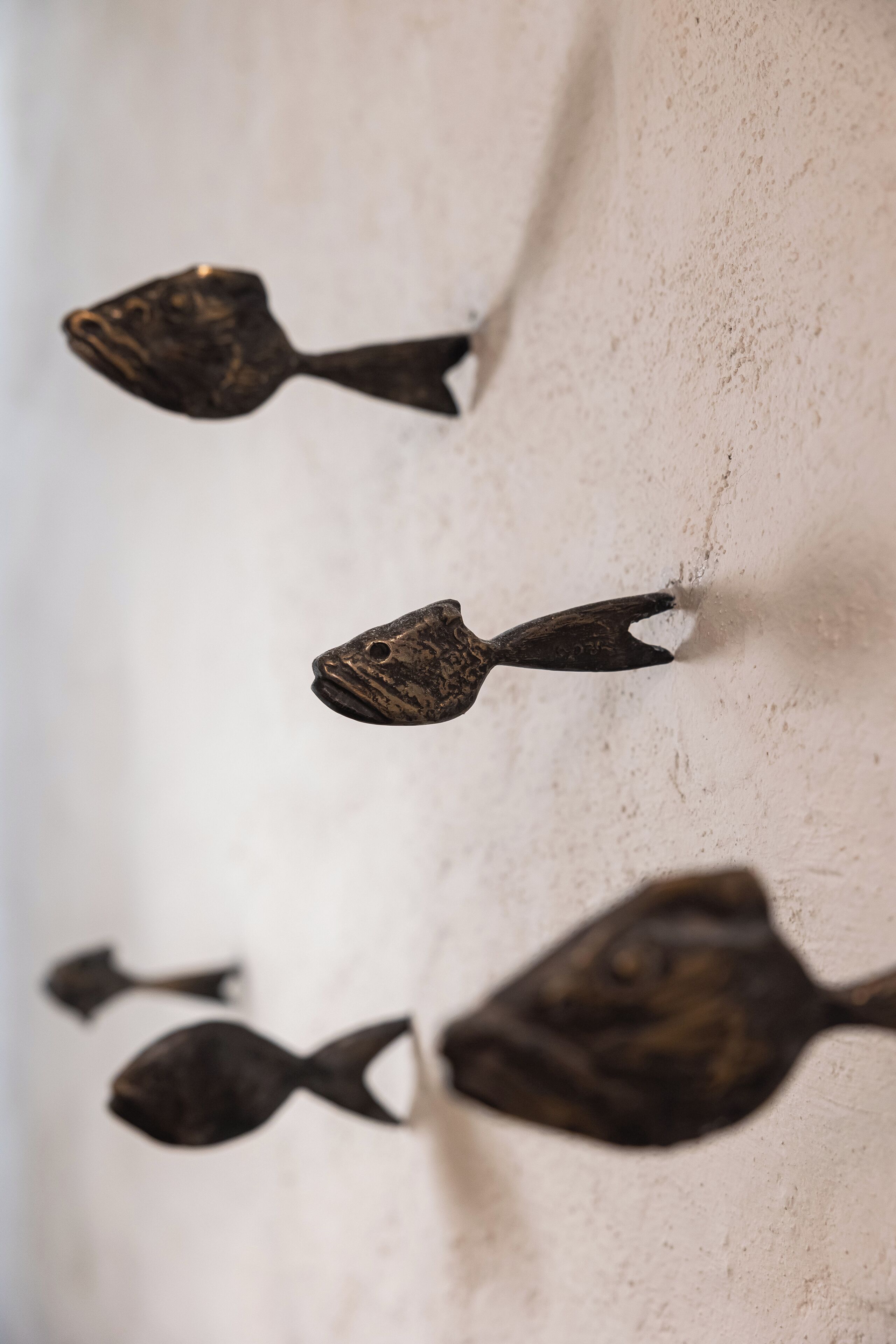 Primer plano de cuatro esculturas metálicas con forma de pez sobre una pared con textura.
