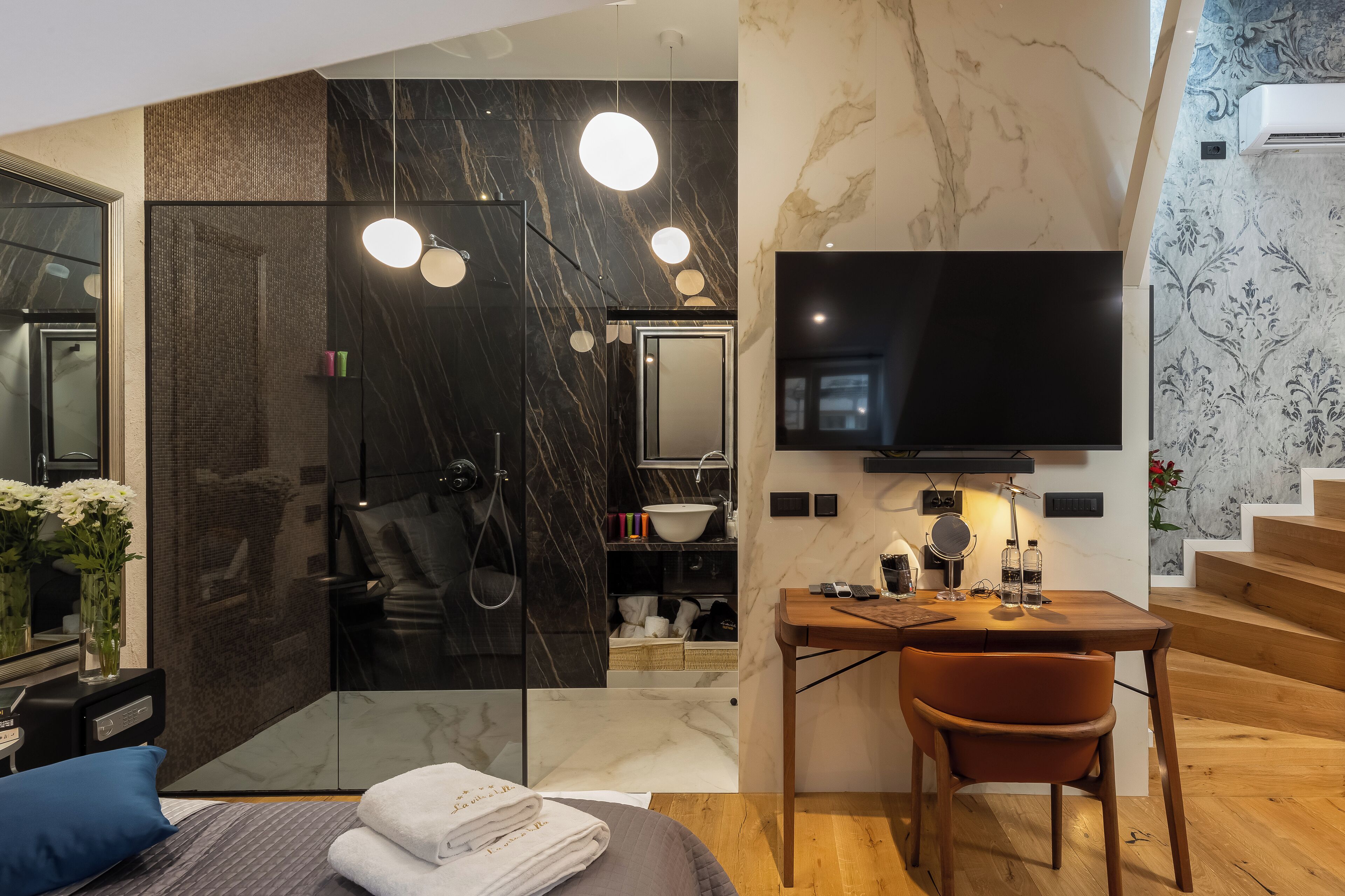 A modern bathroom with a glass shower enclosure, a vanity with a sink, and a flat-screen TV mounted on the wall.