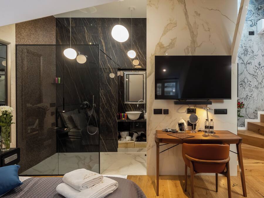 A modern bathroom with a glass shower enclosure, a vanity with a sink, and a flat-screen TV mounted on the wall.