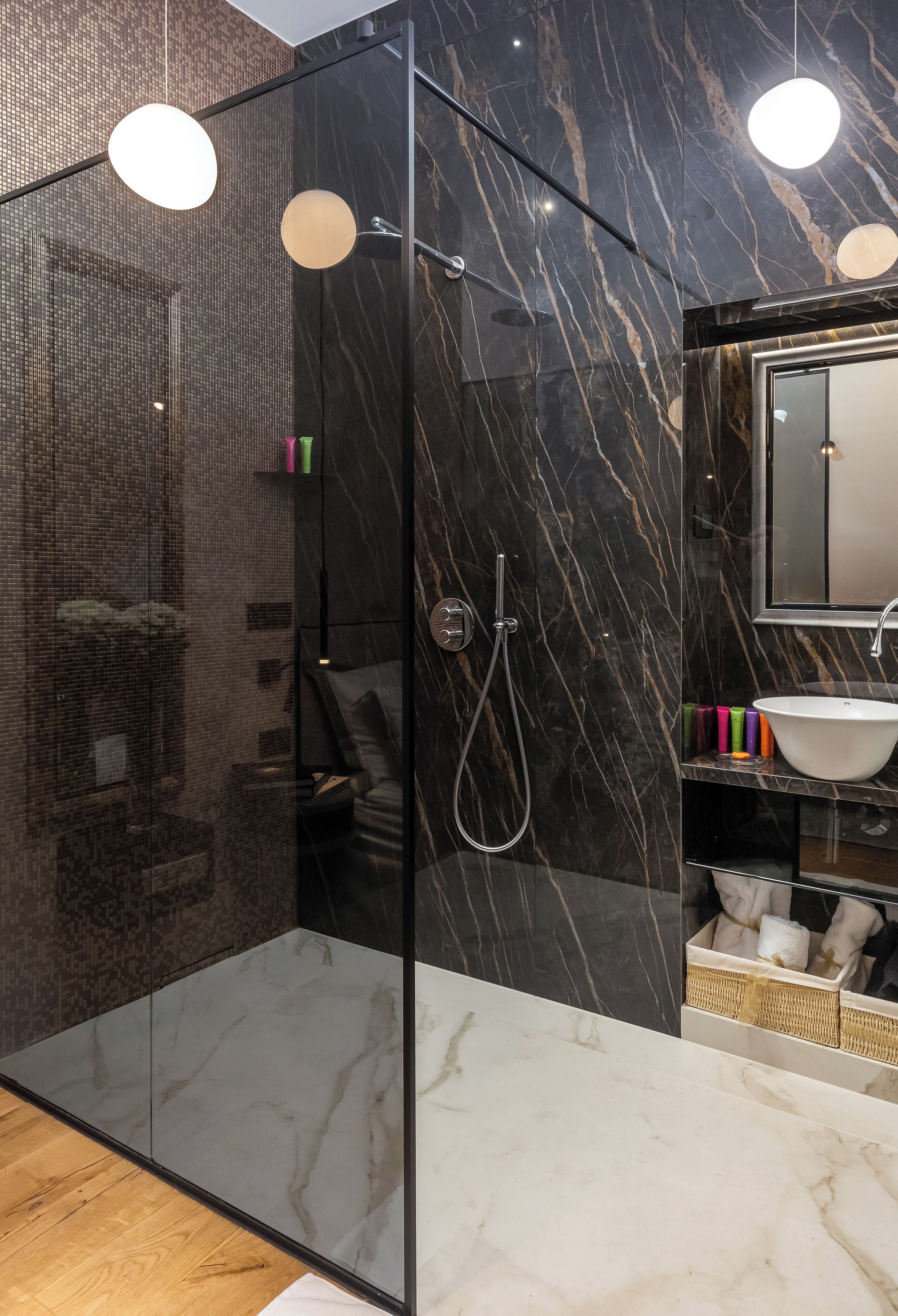 A modern bathroom with a glass-enclosed shower, marble walls, and a white sink.