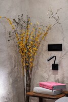 Um painel de interruptores fixado na parede, um vaso com flores amarelas e dois livros sobre uma mesa de madeira.