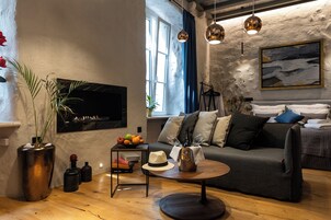Una sala de estar moderna con un sofá, una mesa de centro y una chimenea. Hay una ventana con cortinas, una planta y un cuadro en la pared.