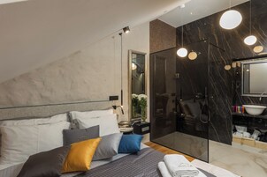 Quarto moderno com cama grande, box de chuveiro de vidro e banheiro em mármore.