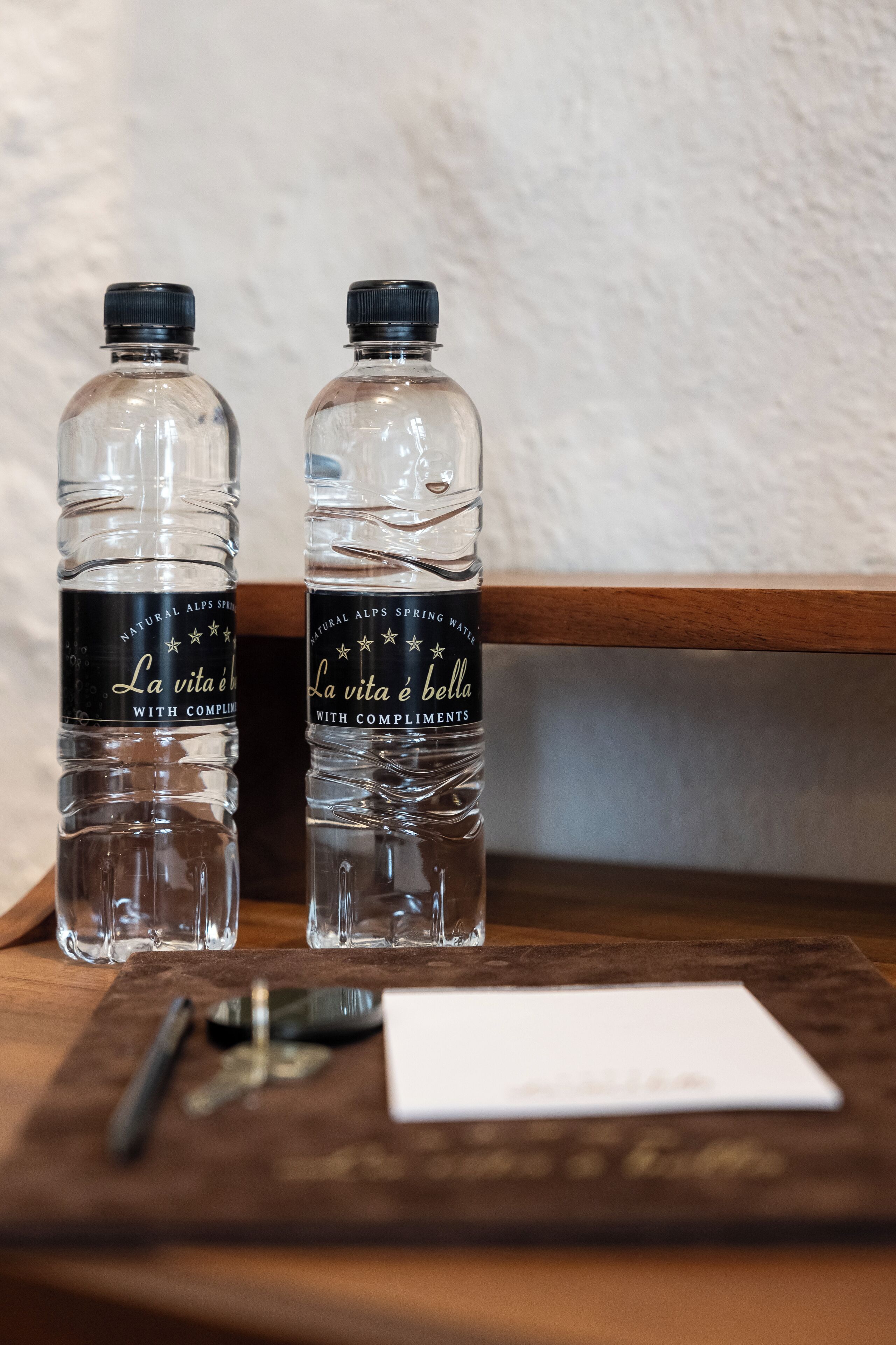 Dos botellas de agua con la etiqueta "La vita è bella" sobre una superficie de madera, junto a llaves y una tarjeta.