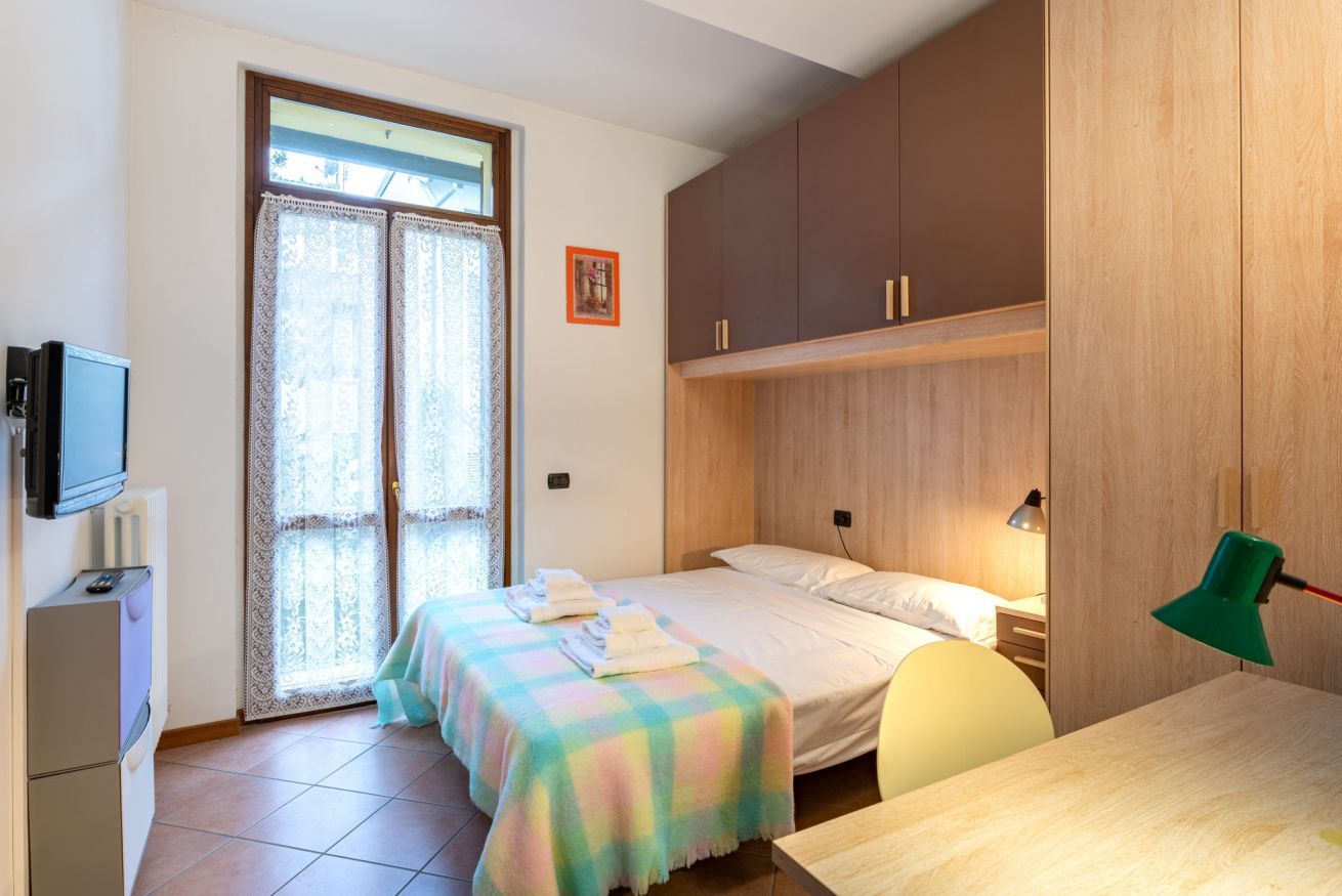 A bedroom with two beds, a desk, a television, and a window with curtains.