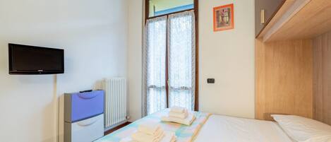 A bedroom with a bed, a television, a radiator, and a window with curtains.