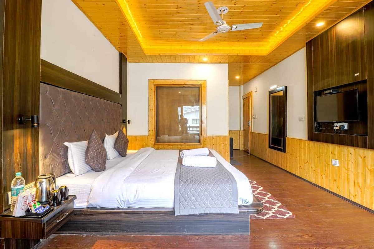 A hotel room with a large bed, wooden walls, a ceiling fan, and a TV on the wall.