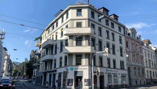 A corner building with multiple floors, a storefront on the ground floor, and a tram line in front. - VISIONAPARTMENTS Zurich Brandschenkestrasse (Zürich)
