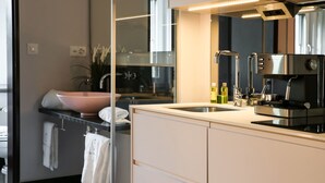 A modern kitchen with a stainless steel espresso machine, a pink sink, and a glass backsplash. - VISIONAPARTMENTS Zurich Brandschenkestrasse (Zürich)