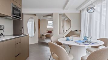Eine moderne Küche mit eingebauten Geräten, ein Essbereich mit rundem Tisch und Stühlen sowie ein Blick durch ein Fenster.