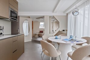 Eine moderne Küche mit eingebauten Geräten, ein Essbereich mit rundem Tisch und Stühlen sowie ein Blick durch ein Fenster.