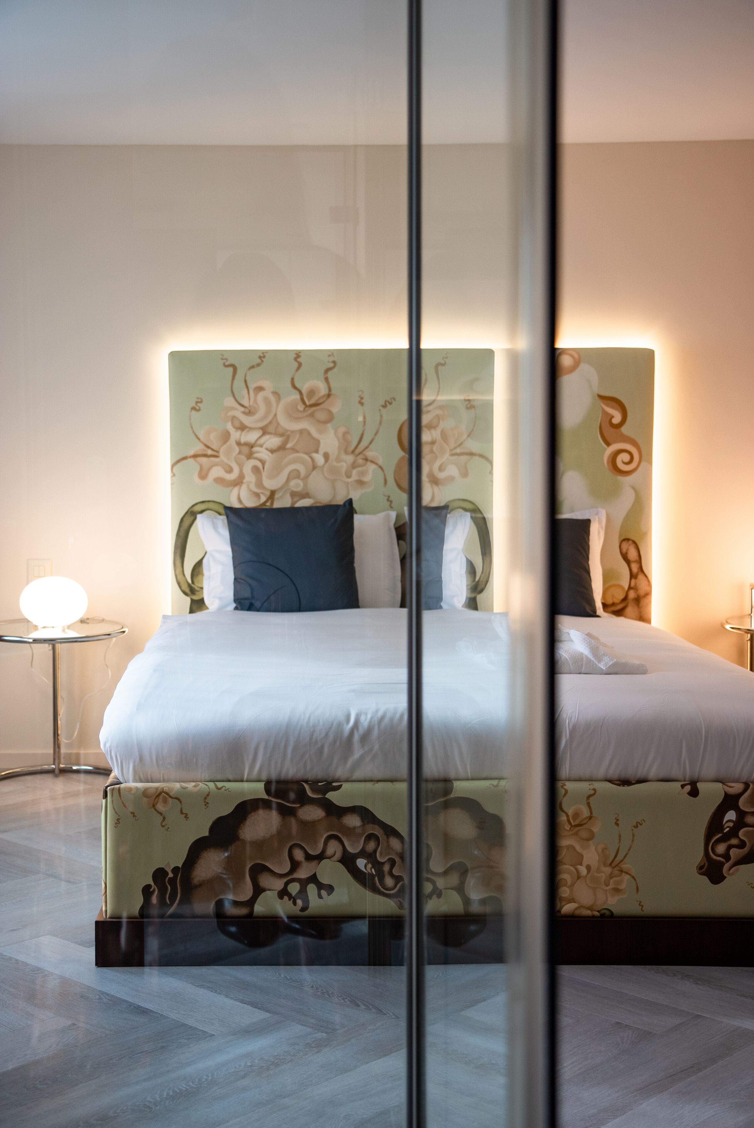 Ein modernes Schlafzimmer mit einem großen Bett, einer Glastrennwand und einem runden Tisch mit einer Lampe.