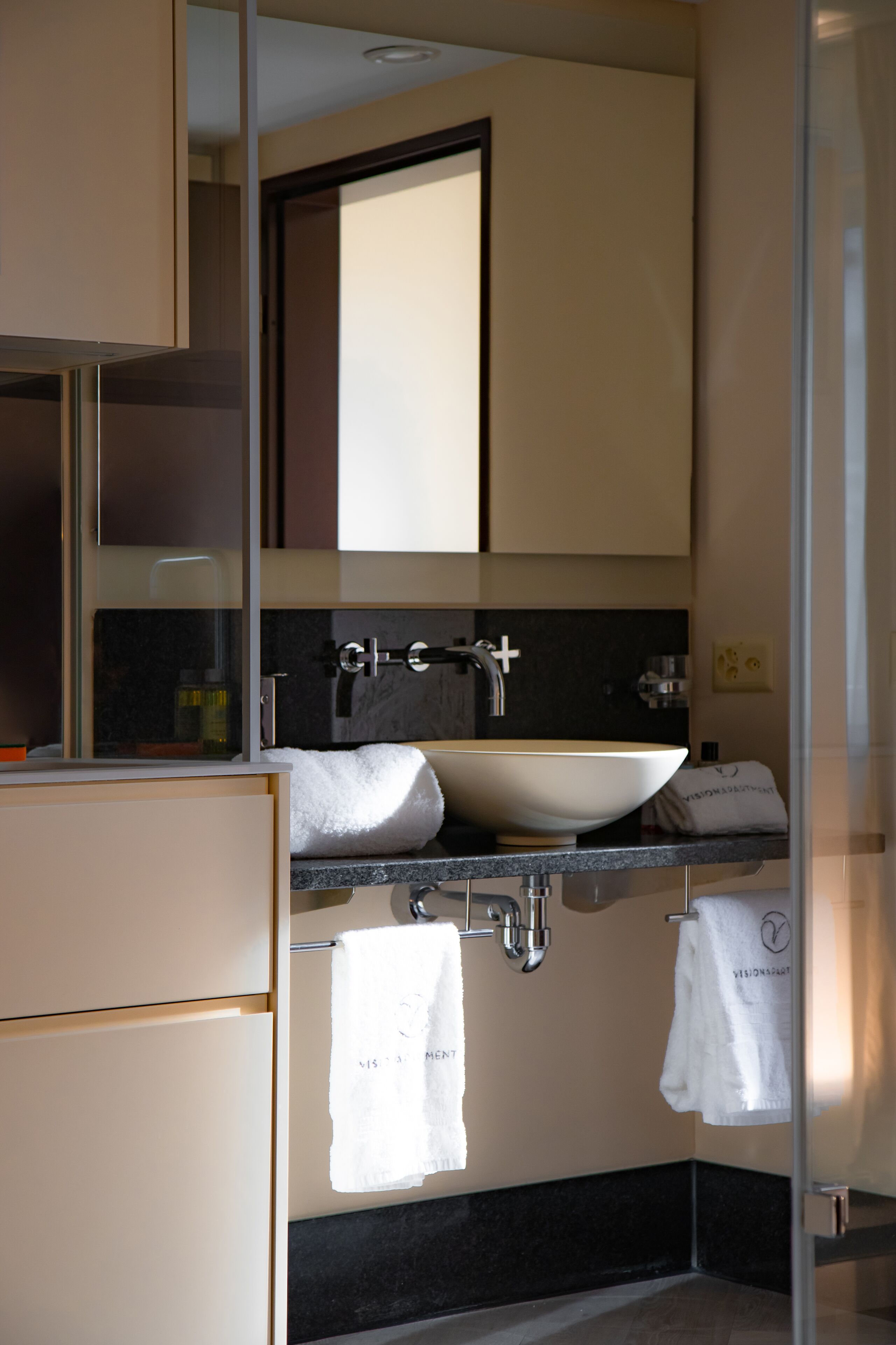 Ein modernes Badezimmer mit einem großen Spiegel, einem weißen Waschbecken und zwei Handtüchern, die an Haken hängen.