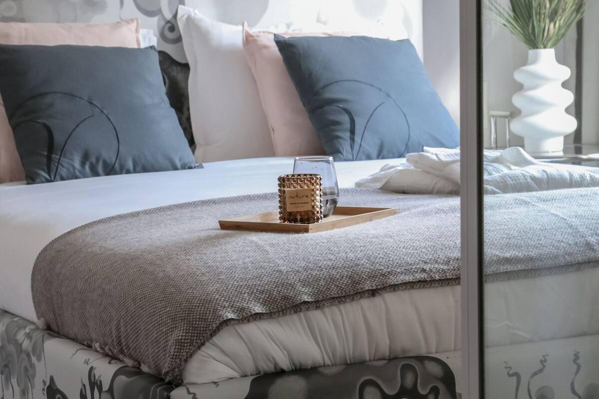 Une chambre à coucher moderne avec un lit doté d’une tête de lit au design original, une table de chevet ornée d’un vase de fleurs et un lit parfaitement fait, sur lequel se trouve un plateau avec divers objets.