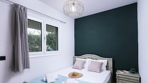 Une chambre à coucher comprenant un lit, une table de chevet, une fenêtre avec des rideaux et un luminaire suspendu.