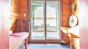 Una baita di legno con una porta scorrevole in vetro che dà su un patio esterno. All'interno, c'è un letto con una coperta rossa, un tavolino e una maschera decorativa appesa al muro.