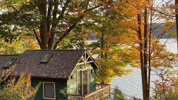 Una baita con facciata verde, un piccolo balcone e vista su un lago.