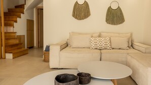 A modern living room with a wooden staircase, a beige sofa, a round coffee table, and wall-mounted macramé decorations. - PAPADRIA VILLAS as featured in THE TIMES - Modern Luxury Getaway nr Kathisma (Tsoukalades)