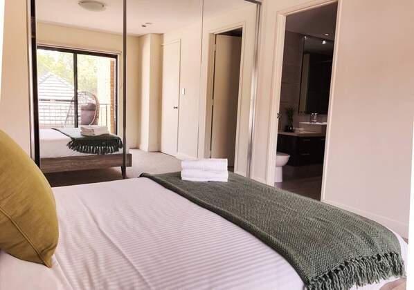 A hotel room with a bed, a green throw blanket, and a view of the bathroom and outside.