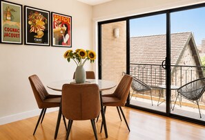 A dining area with a round table, four chairs, a vase with sunflowers, and a large sliding glass door leading to an outdoor balcony.