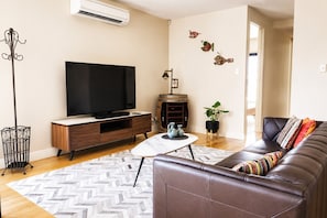 Un salon moderne doté d’un téléviseur à écran plat, d’un meuble de rangement en bois, d’une table basse, d’un canapé et d’œuvres d’art décoratives murales.
