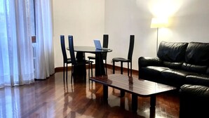 Un salon moderne avec un canapé en cuir noir, une table basse en bois et un ordinateur portable posé sur une petite table.