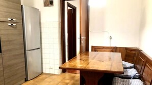 Une cuisine avec une table et un banc en bois, un réfrigérateur et un mur recouvert de carreaux.