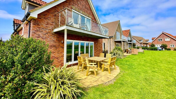 A two-story house with a brick exterior, large glass windows, and a balcony. - Stunning SEAVIEW Coastal Cottage - Sleeping 8 in 4 Bedrooms - Pool and Beach Access Included. (Filey)