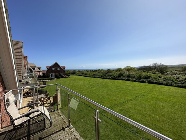 A balcony with a view of a well-maintained lawn and a distant house. - Stunning SEAVIEW Coastal Cottage - Sleeping 8 in 4 Bedrooms - Pool and Beach Access Included. (Filey)