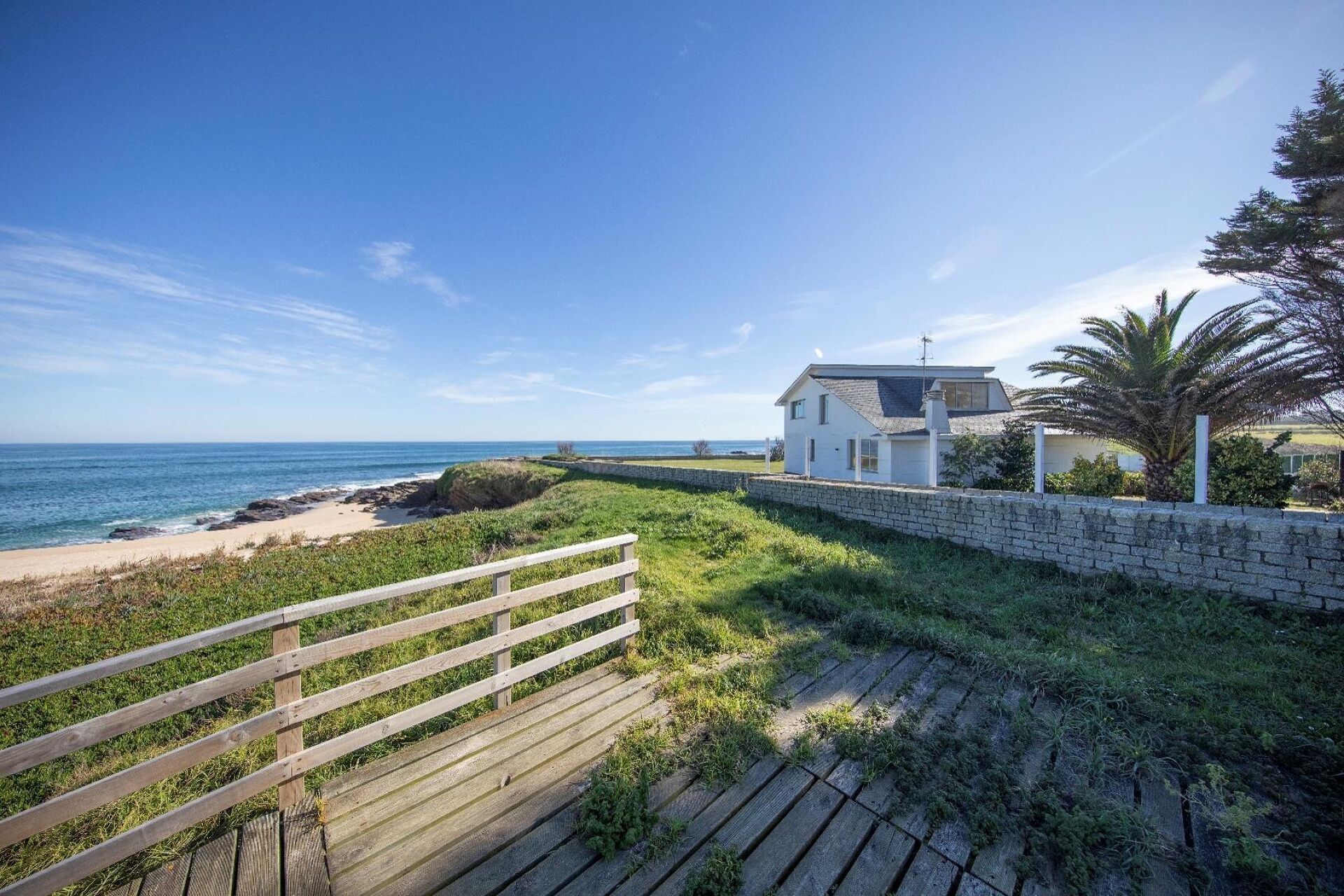 A coastal property with a wooden deck, a stone wall, and a view of the ocean.