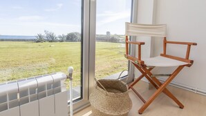 A room with a large window overlooking a grassy field, a director's chair, and a woven basket. - HOUSE ON THE BEACH, FOZ (Unknown)