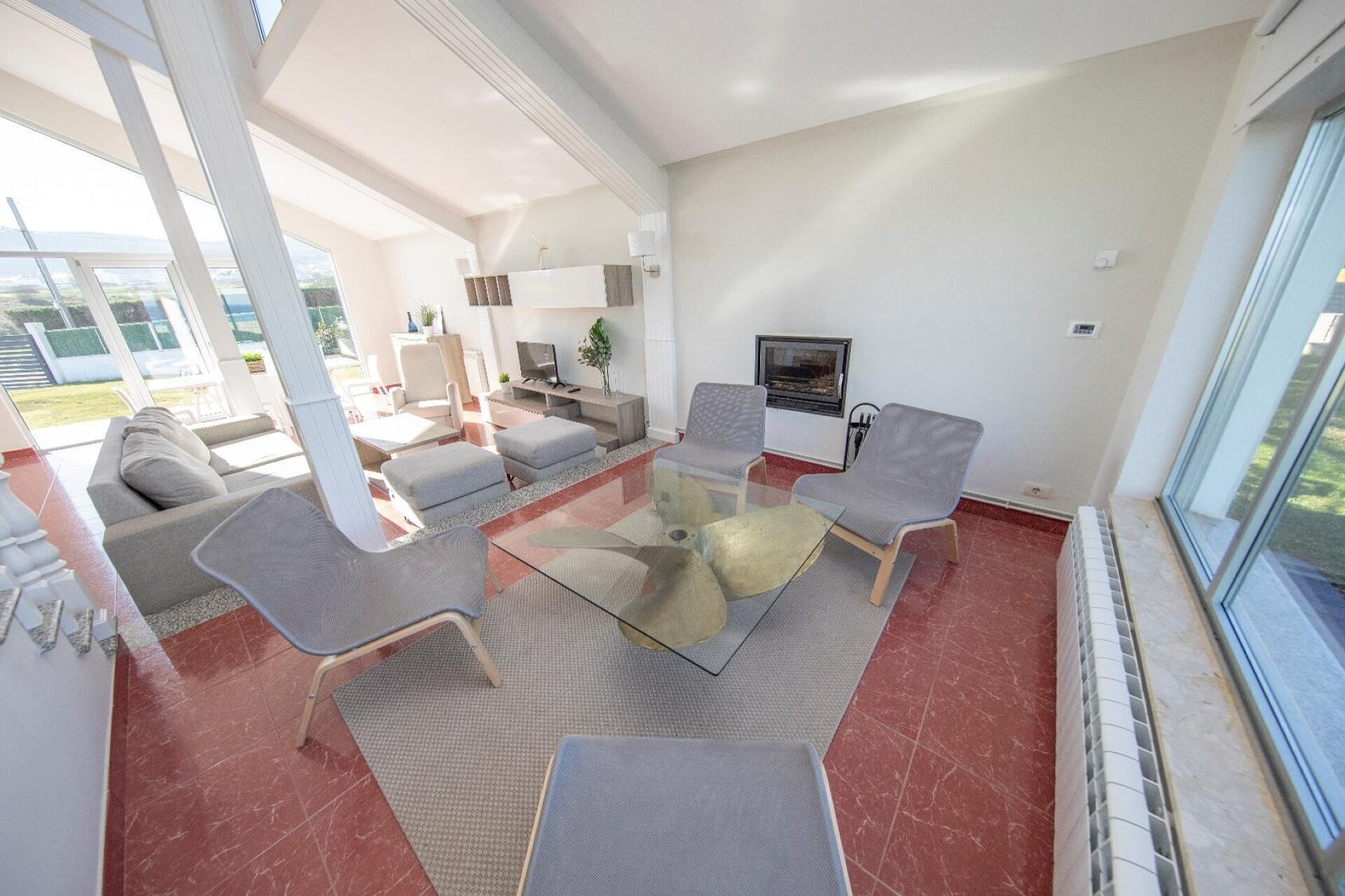 A modern living room with a glass coffee table, grey upholstered chairs, a sofa, and a TV.