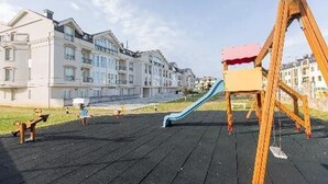 Un parque infantil con tobogán y columpios, rodeado de edificios residenciales.