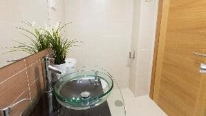 Un baño con lavamanos de vidrio, una planta en maceta y una puerta de madera.