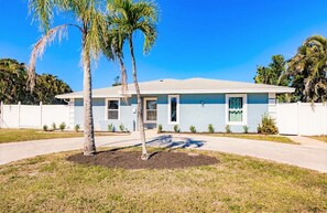 A single-story house with a light blue exterior, a front porch, and a small front yard with palm trees.
