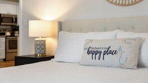 Un lit bien fait, avec un oreiller orné de l’inscription « la plage est mon endroit préféré » et un objet décoratif fixé au mur.