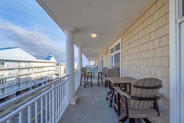 A balcony with a view of a waterfront hotel and a dining area with chairs and a table. - Beautiful 3 Bedroom Condo in North Ocean City with Rooftop Pool (Ocean City)