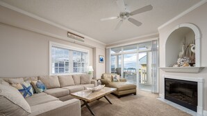 Uma sala de estar ampla com um sofá bege, uma poltrona de couro, uma mesa de centro de madeira e uma lareira.