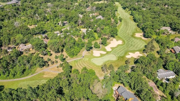 An aerial view of a golf course with sand bunkers, surrounded by dense trees and residential properties.