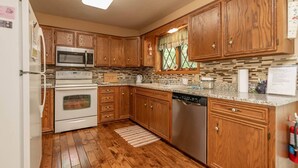 A kitchen with wooden cabinets, a microwave, stove, dishwasher, and a window with a view.